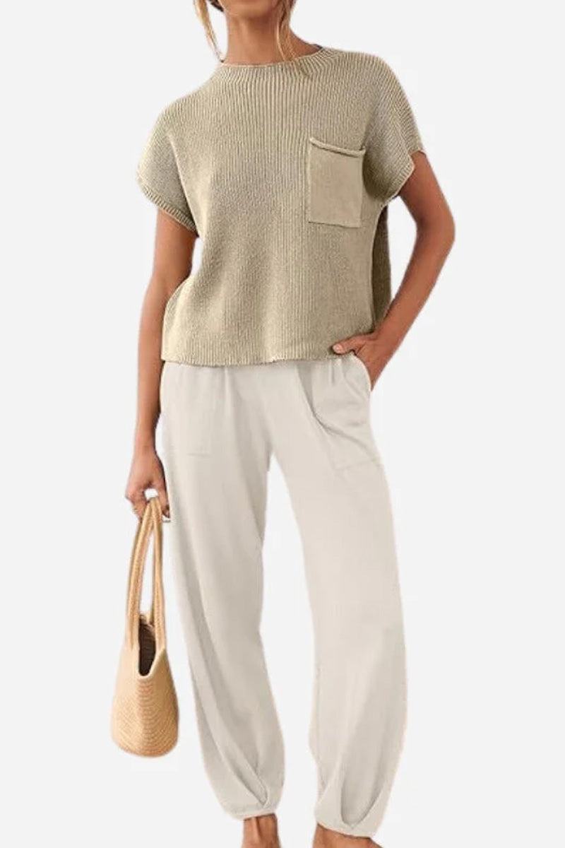 Woman wearing beige Comfy Couture Knit Sweater two-piece set with knit pullover and high-waisted pants, holding a woven handbag.